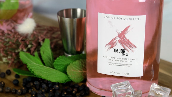 Rectangular clear label applied to a pink gin bottle next to a measuring cup and mint leaves