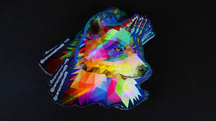 Die cut holographic sticker with geometric wold design against a black background