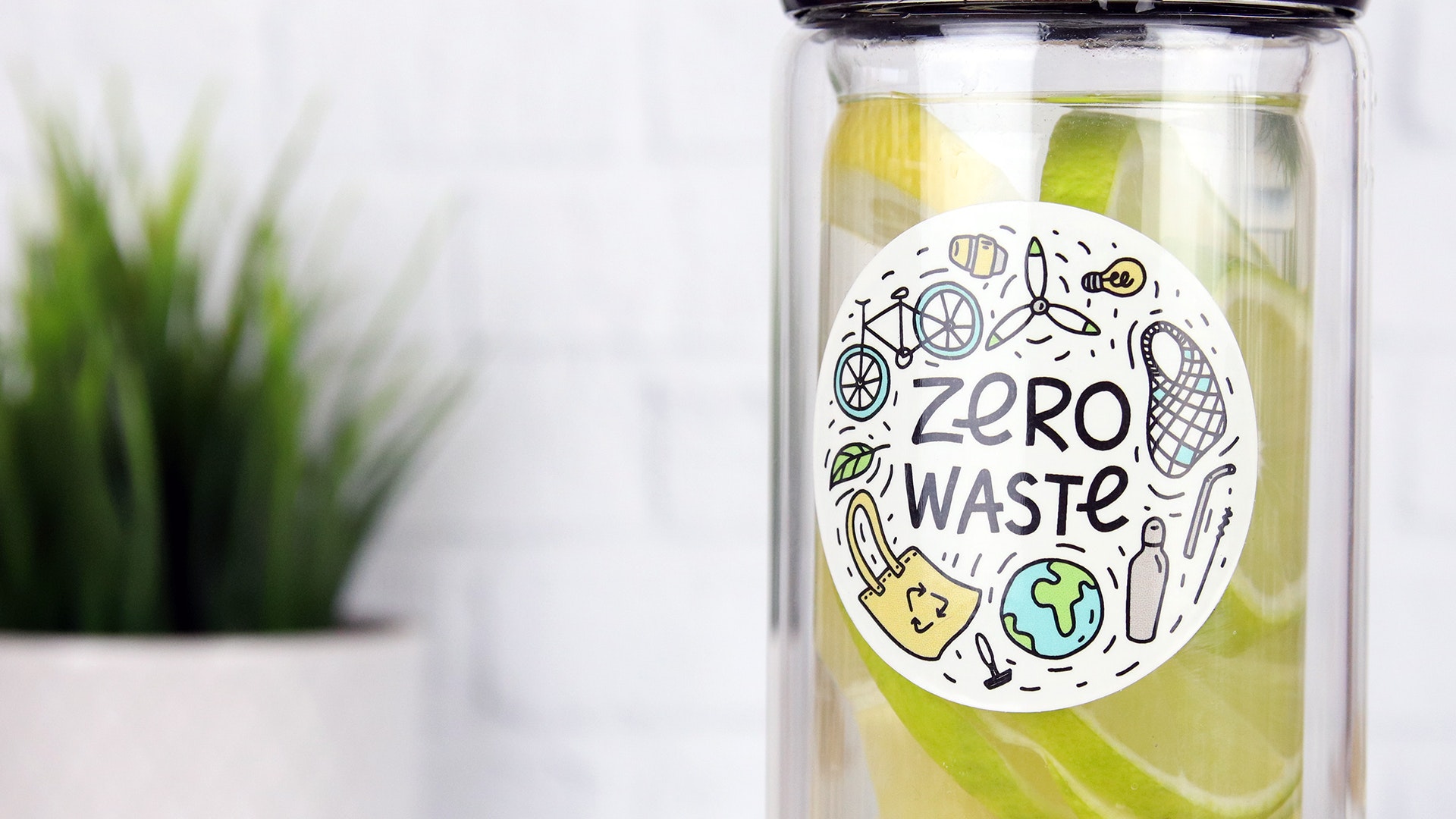 Round eco friendly sticker with zero waste design applied to a glass water bottle filled with lemons and limes