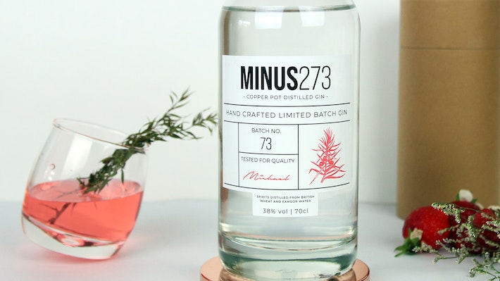 Eco friendly stickers applied to glass gin bottle next to a tilted glass filled with a cocktail
