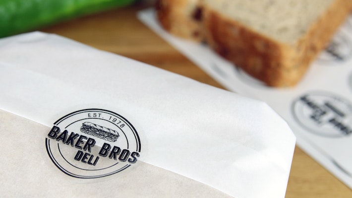 Clear eco friendly label round with baker bros logo applied to seal a sandwich wrapper
