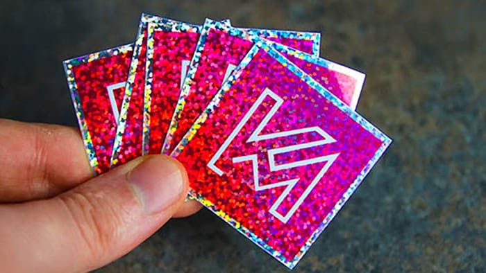 Square glitter stickers with km logo hand held