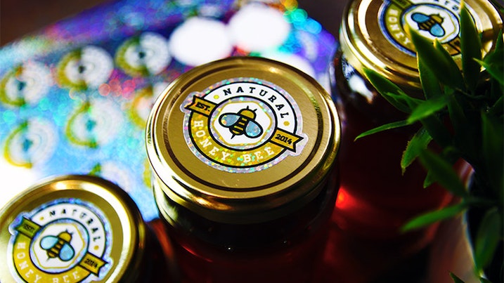 Three die cut glitter stickers applied to different honey jars on a wooden board