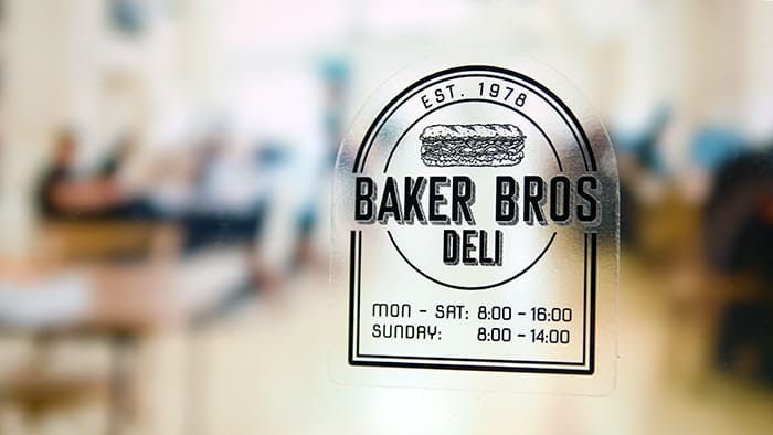 Die cut eco-friendly front adhesive stickers with Baker Brows Deli logo applied to a window