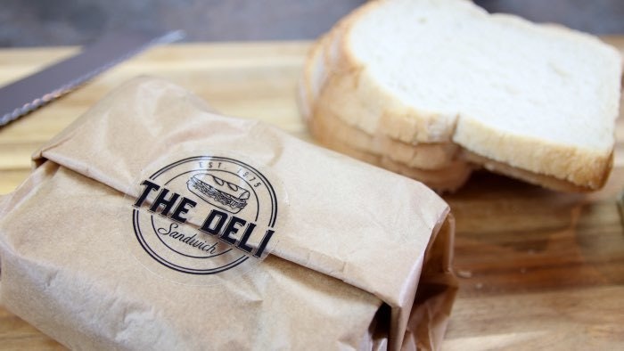 Circle eco-friendly clear stickers with a deli logo applied to seal a sandwich wrap