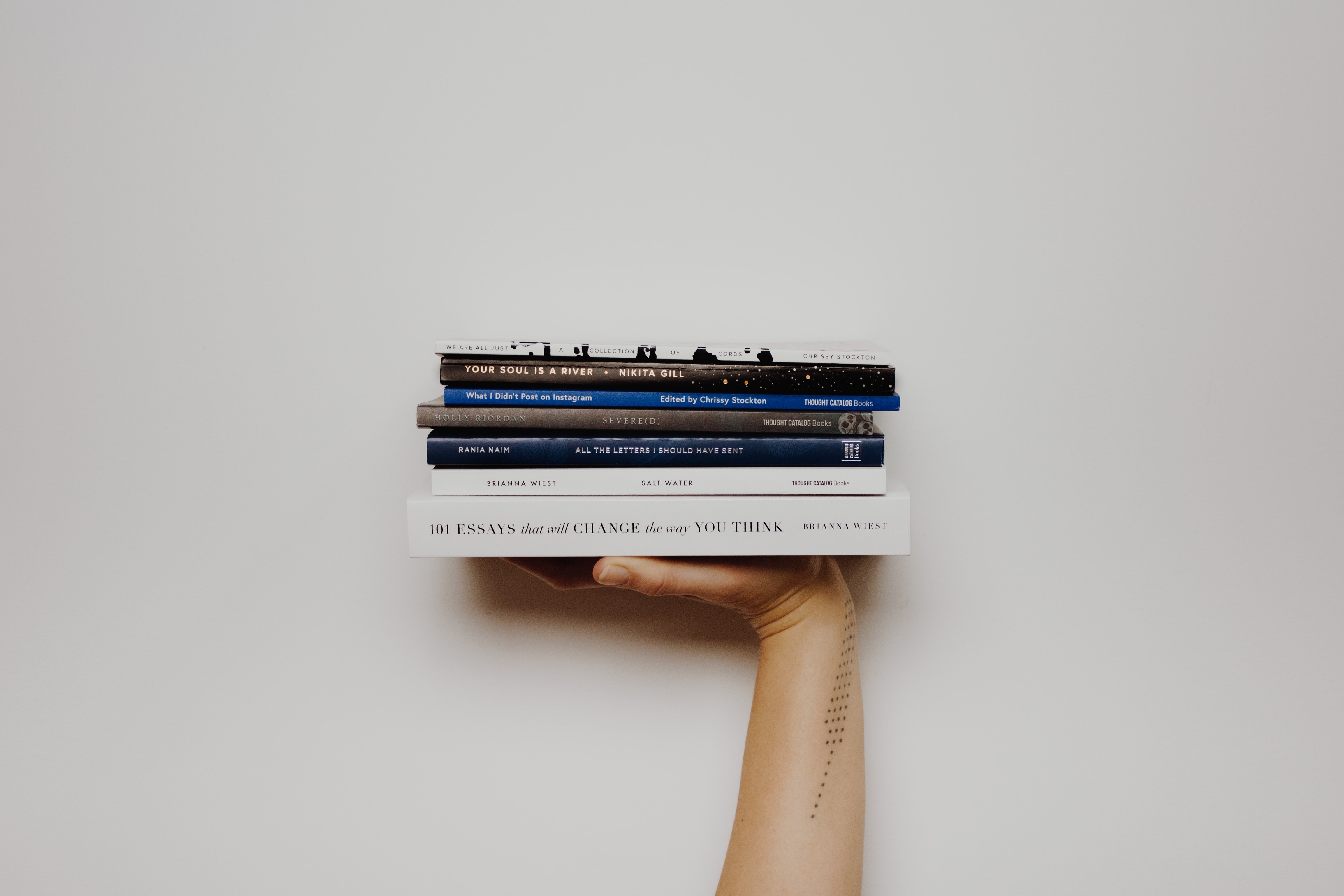 A pile of books being held by a hand against a white wall