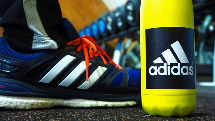 Square white vinyl stickers with Adidas logo applied to a yellow water bottle in the gym