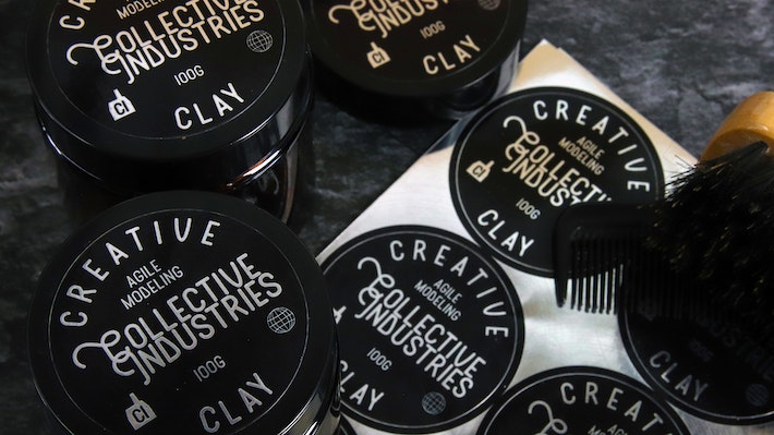 Circle mirror silver labels applied to black tins containing hair care next to a sticker sheet