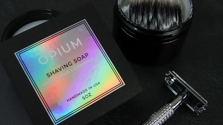 Square holographic sticker applied to black soap box next to shaving tools