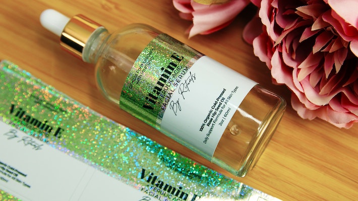 Sheet of rectangle eco-friendly glitter labels with vitamin e design and one label applied to a glass bottle
